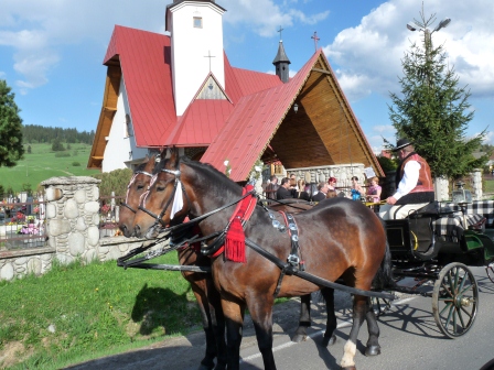 Horse with red collar pulling a wagon with driver sitting in front of a church