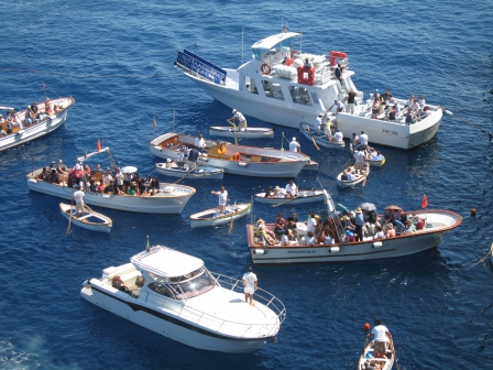 6 large white boats in close quarters surrounded by small rowboats on blue water