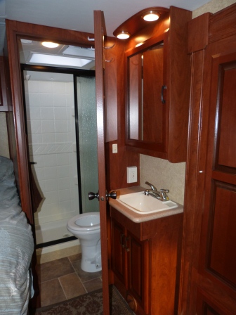Bathroom with open door showing shower and toilet.  Vanity outside.