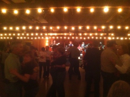 The Almost Patsy Cline Band on stage with strings of white lights abvoe and couples dancing in the dark foreground